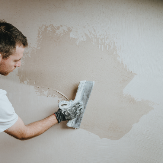 Male builder in work overalls plastering a wall using a construction trowel. Horizontal panorama banner with blank space for text.