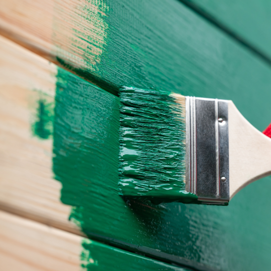 Painting outdoor house wall with a brush. Man painting wooden wall in green color, renovating house, new facade